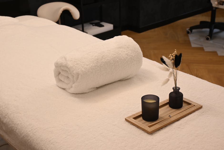 A serene spa massage table setup with a rolled towel, candle, and decorative vases in a relaxing environment