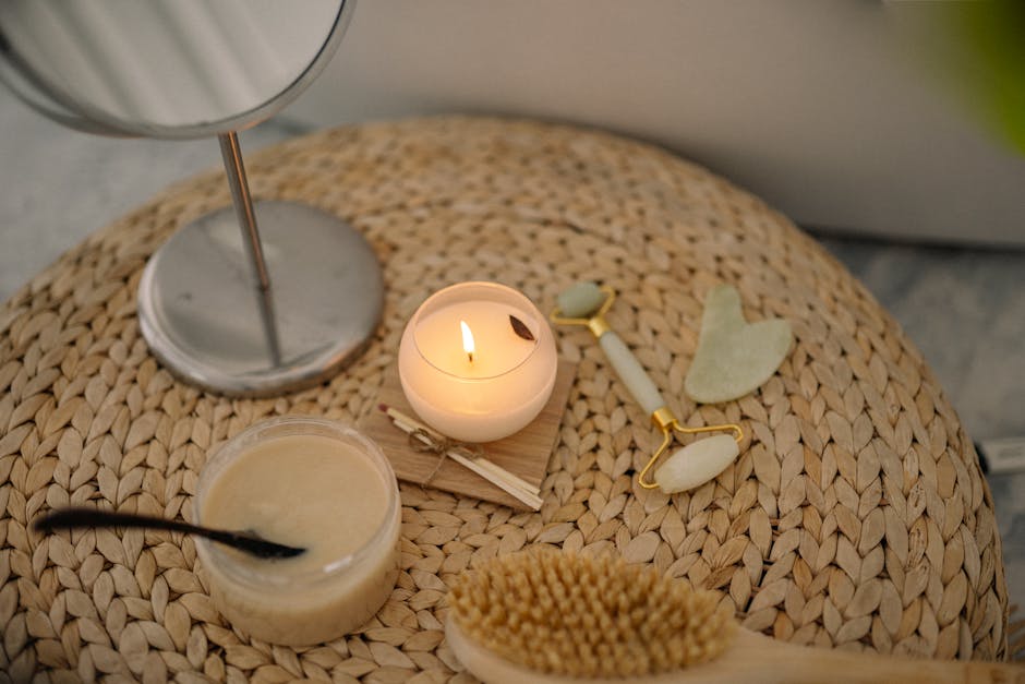 A serene spa setup featuring a lit candle, jade face roller, and body scrub on a woven mat