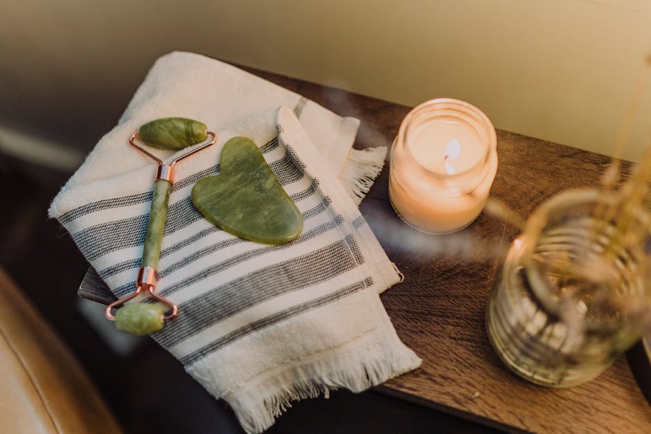 Calming spa setup featuring a jade roller, gua sha stone, and candle for relaxation and skincare
