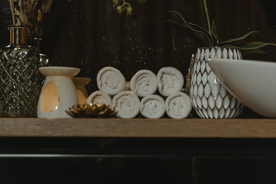 Serene spa setting featuring rolled towels, candlelight, and decorative vases on a wooden shelf